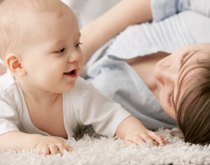 A Mother lying on a carpet playing with her crawling baby