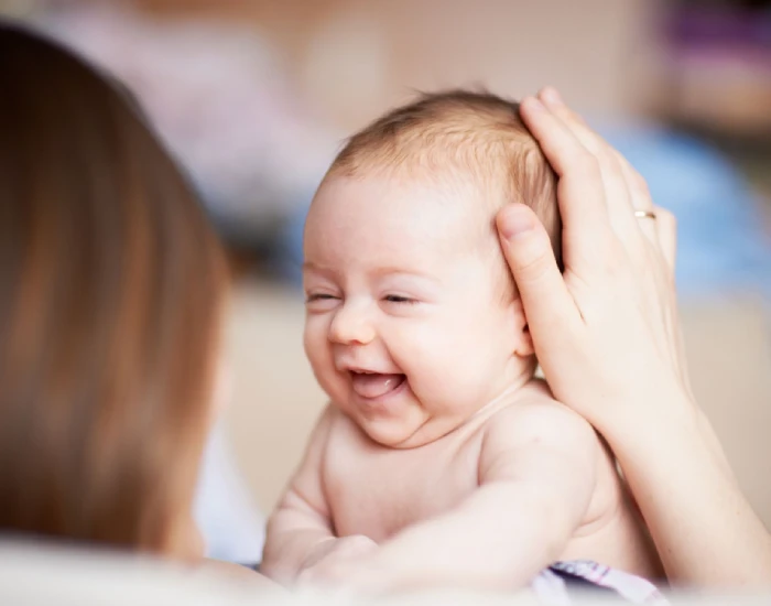 A mother holding her smiling cute baby with her left hand on the baby’s head