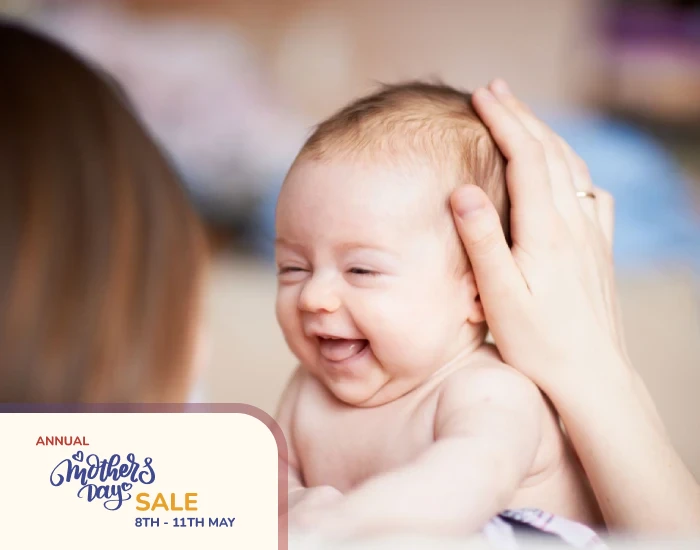 A mother holding her smiling cute baby with her left hand on the baby’s head