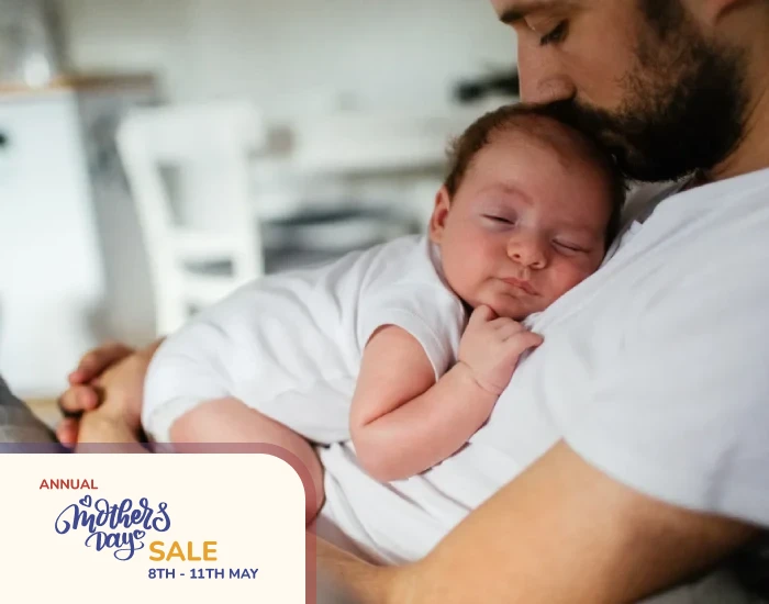 A father kissing his baby on his head while the baby is sleeping on his father’s chest